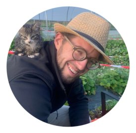 Flo souriant porte un chaton sur son épaule, créant un moment chaleureux et amical en cueillant des fraises.