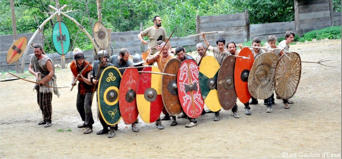 Des hommes se tenant ensemble avec des boucliers coloriés et des lances, évoquant un esprit de camaraderie et de force.