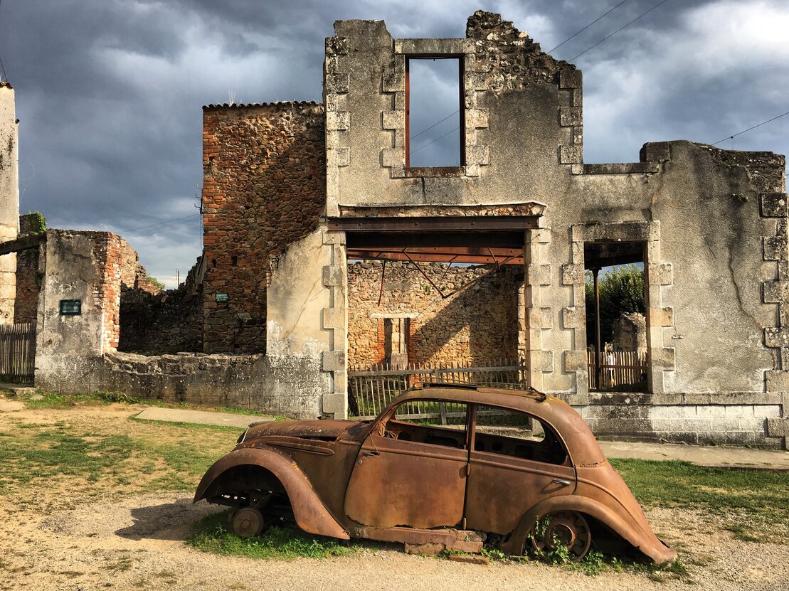 Un vieux véhicule rouillé est stationné devant un bâtiment, créant une atmosphère de désuétude et de mémoire.